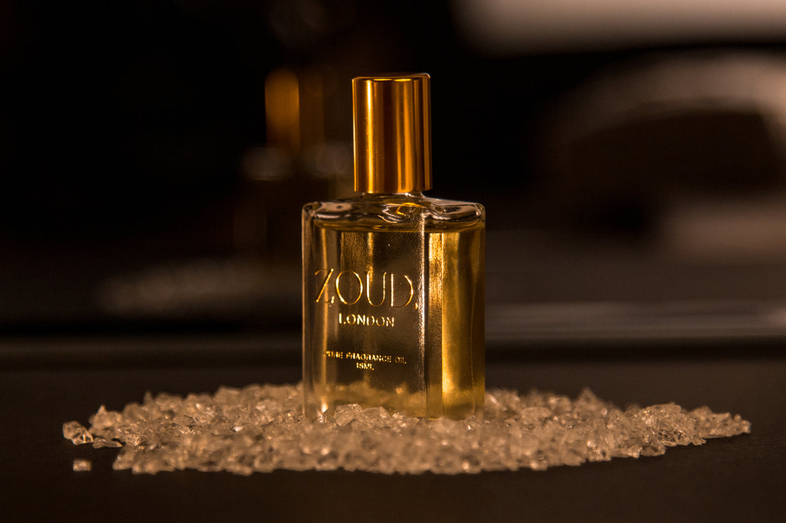 A bottle of Moresqe Elixir perfume oil with a gold cap, surrounded by scattered crystals on a dark surface.